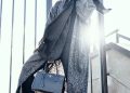 woman in gray coat holding black handbag standing on gray stairs during daytime