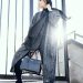 woman in gray coat holding black handbag standing on gray stairs during daytime